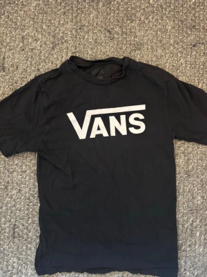 Svart Vans t-shirt med logga - Svart t-shirt från Vans med stor vit logga tryckt på bröstet. Klassisk rak passform och rund halsringning. Perfekt för dig som gillar streetwear och vill ha en enkel men snygg tee.
