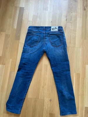 Jacob cohen jeans - Säljer ett par klassiska blå jeans från jacob cohen med raka ben och femficksmodell. Jeansen har snygga slitningar framtill och bakfickor med diskreta sömmar. Materialet är kraftig denim i bomull. Perfekta för en stilren och avslappnad look.