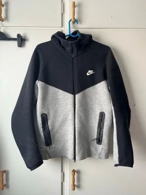Nike hoodie svart och grå M - Nike hoodie i svart och grått med dragkedja framtill och två fickor med dragkedja. Klassisk Nike-logga på bröstet och huva. Tillverkad i mjukt material som passar perfekt för en chill look.