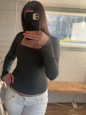 Mörkgrå ribbad långärmad topp - Snygg mörkgrå ribbad topp med lång ärm och fyrkantig ringning. Figurnära passform som passar perfekt till både jeans och kjol. Enkel och stilren design, perfekt för lager-på-lager eller som den är.