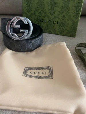 Svart GG-mönstrat bälte  - Snyggt svart bälte från med klassiskt GG-mönster och stor silverfärgad logga som spänne. Bältet är gjort i skinn och har en exklusiv känsla, perfekt för att lyfta vilken outfit som helst.