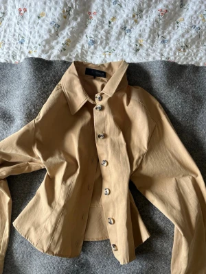 Beige skjorta med knappar från Zara - Säljer en beige skjorta från Zara med klassisk krage och stora knappar framtill. Skjortan har långärmad design och är tillverkad i bomull. Snygg passform som ger en stilren look.