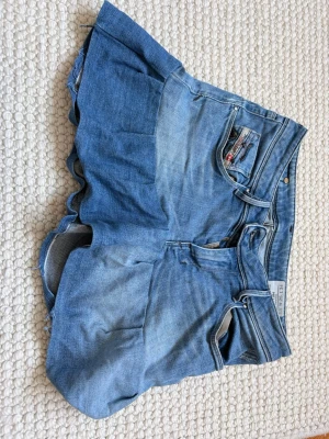 Blå jeanskjolmed volang - Unika blå jeanskjol från ELLE JEANS med volangdetalj längs benen. Klassisk femficksdesign och knappstängning framtill. Kjolens denim är i en ljusblå ton och har en cool, avslappnad passform. Har inga defekter och skriv för mer bilder. 