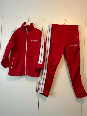 Rött tracksuit från Angels - Rött tracksuit-set från Angels med vita ränder längs ärmar och ben. Jackan har dragkedja, ståkrage och två fickor. Den kommer ej till användning därför säljer jag tracksuiten. Pris kan diskuteras!