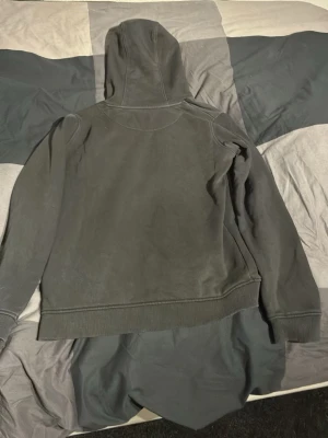 Svart hoodie från Lyle & Scott - Svart hoodie från Lyle & Scott med klassisk gul logga på bröstet. Hoodien har huva med dragsko och en stor känguruficka framtill. Tillverkad i mjukt bomullsmaterial och har ribbade muddar vid ärmslut och nederkant. Perfekt för en avslappnad och stilren look.