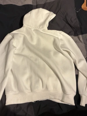 Vit hoodie från C.P. Company - Säljer en vit hoodie från C.P. Company med ikoniska glasögon i huvan. Hoodien har dragkedja, ribbade muddar och är tillverkad i mjukt material. Perfekt för dig som vill sticka ut med en unik detalj på huvan.