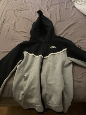 Nike tvåfärgad hoodie med dragkedja - Snygg hoodie från Nike i svart och grått med vit logga på bröstet. Hoodien har dragkedja framtill, fickor på sidorna och en stor huva. Tillverkad i mjukt sweatshirtmaterial som är perfekt för chill eller träning. Klassisk sportig look med kontrastfärger.