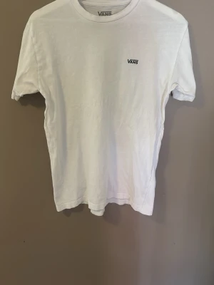Vit t-shirt från Vans - Klassisk vit t-shirt från Vans i bomull med liten Vans-logga på bröstet. Modellen är kortärmad och har en rund halsringning. Perfekt basic-plagg att ha i garderoben.