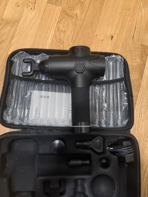 Svart massagepistol med tillbehör - Massagepistol i svart plast med flera utbytbara munstycken och laddare, levereras i en praktisk förvaringsväska. Perfekt för att mjuka upp muskler och ge djupgående massage. Ergonomiskt handtag och enkel att använda.
