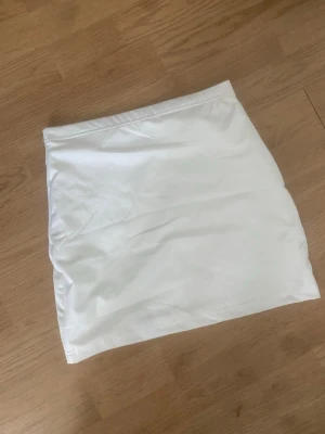 Vit kortkjol i bomull - Snygg vit kortkjol i enkel och stilren design. Kjolen har rak passform och är tillverkad i mjukt bomullstyg, perfekt för en fräsch och clean look. Lätt att matcha med olika toppar och accessoarer.
