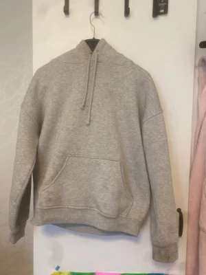 Grå basic hoodie med ficka - Enkel och stilren grå hoodie med huva och dragsko. Har en stor magficka framtill och ribbade muddar vid ärmslut och nederkant. Perfekt för en avslappnad och casual look.