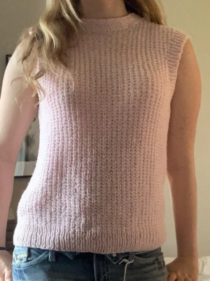 Ljusrosa stickad ärmlös topp - Säljer en ljusrosa stickad topp utan ärmar. Toppen har en ribbad struktur och rund halsringning. Perfekt att styla med jeans eller kjol för en trendig look. Materialet känns mjukt och bekvämt mot huden.
