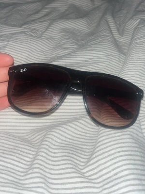 Ray-Ban svarta solglasögon - Säljer ett par klassiska svarta solglasögon från Ray-Ban med bred båge och mörktonade glas. Snygg och tidlös modell som passar till alla outfits. Ray-Ban-loggan syns tydligt på båda sidorna av bågen.