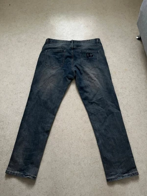 Mörkblå jeans från Dolce & Gabbana - Snygga mörkblå jeans från Dolce & Gabbana med raka ben och klassisk femficksdesign. Bakfickan har en broderad DG-logga och text. Jeansen är i denim och har en cool, lite tvättad look som passar perfekt till streetwear.