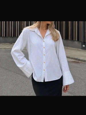Skräddad vit skjorta i 100% Bomull - Nikolay d'Etoiles - kräddad skjorta fràn Nikolay d'Etoiles med en elegant silhuett och samtidigt en avslappnad, lätt oversized känsla. Modellen är fint formad med lätt utsvängda ärmar och en subtil markering i midjan som ger ett valdigt smickrande fall. Tyget känns otroligt lyxigt mot huden med en slät, nästan strykfri känsla som ger hela plagget ett exklusivt och välklätt uttryck. 100% bomull. Som ny. Stl 36