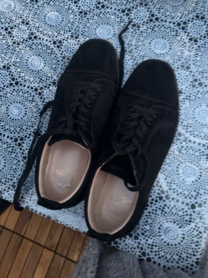 Svarta Louboutin sneakers med röd sula - Snygga svarta sneakers från Christian Louboutin med klassisk röd sula och svarta skosnören. Skorna är använda ett par gånger men de funkar precis som om de var helt nya ! Vid snabbköp kan pris diskuteras annars ber jag alla ge rimliga priser! 