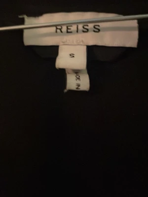 Svart hoodie från Reiss - En stilren svart cardigan från Reiss i storlek S. Den har en klassisk passform med huva och långa ärmar. Perfekt för en avslappnad och trendig look. Materialet känns mjukt och bekvämt mot huden.