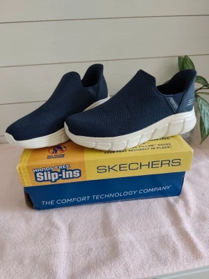 Blå Skechers Slip-ins sneakers - helt nya. - Nya oanvända skor, Mörkblå slip-in sneakers från Skechers med vit, chunky sula och ventilerande mesh-ovandel. Skorna har en sportig look och är enkla att ta på tack vare handsfree-designen. Perfekta för dig som gillar bekväma och stilrena sneakers. Ordpris 1200 kr. 