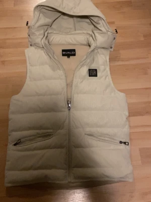 Beige väst från Bvaldi med huva - Snygg beige dunväst från Bvaldi med avtagbar huva. Kontakta mig vid fler frågor. Köp kan diskuteras vid enkel affär. Använd fåtal gånger 