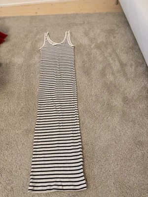 Randig långklänning i ribbad bomull - Ribbad långklänning från H&M i storlek XS. Klänningen är vit med svarta horisontella ränder och har ärmlös design med rundad halsringning.