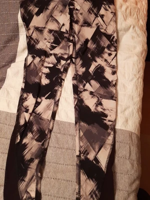 Svarta och beige mönstrade leggings - Snygga leggings med abstrakt svart och beige mönster. De har en tight passform och är gjorda i ett stretchigt material som passar perfekt för både träning och chill. Sidopaneler i helsvart ger en cool kontrast till det grafiska mönstret.