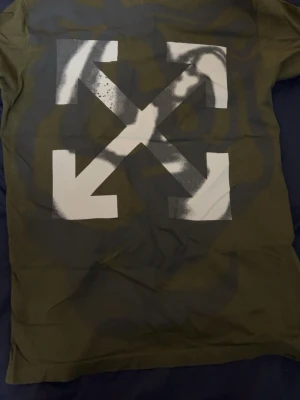 Grön Off-White t-shirt med tryck - Cool grön t-shirt från Off-White med det ikoniska vita pilar-trycket på ryggen. T-shirten har klassisk passform och är tillverkad i mjuk bomull. Perfekt för dig som gillar streetwear och vill sticka ut.