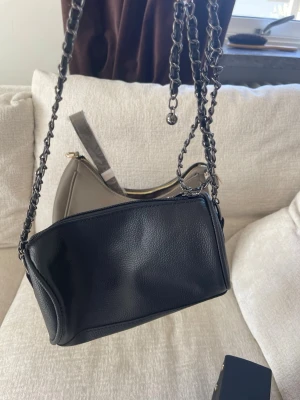 Beige axelväska i minimalistisk design - Snygg beige axelväska med stilren och enkel form. Väskan har en mjuk struktur och är tillverkad i slätt syntetmaterial. Guldiga detaljer vid dragkedjan och en praktisk axelrem. Perfekt för dig som gillar en clean look och vill ha plats för det viktigaste.