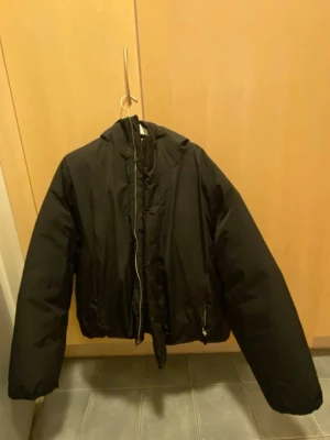 Svart pufferjacka från Bershka - Snygg svart pufferjacka från Bershka med dragkedja och hög krage. Jackan har en klassisk boxig passform och är vadderad för extra värme. Perfekt för kalla dagar och enkel att matcha med olika outfits. Går ej att stänga med dragkedja utan med kardborre!