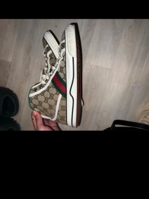 Gucci beige monogram sneakers - Snygga sneakers från Gucci i beige canvas med klassiskt GG-monogram, gröna och röda ränder på sidan samt vita detaljer. Skorna har vita snören och grön insida för en extra touch. Perfekta för dig som vill sticka ut med lyxig streetstyle. Skorna går för cirka 8000 på affär. Pris kan diskuteras så tveka inte på att höra av er.