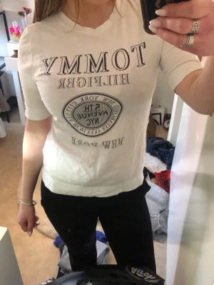 Vit Tommy Hilfiger t-shirt New York - Snygg vit t-shirt från Tommy Hilfiger med tryck framtill. Klassisk passform med korta ärmar och rund halsringning. Perfekt till jeans eller shorts för en clean och stilren look.