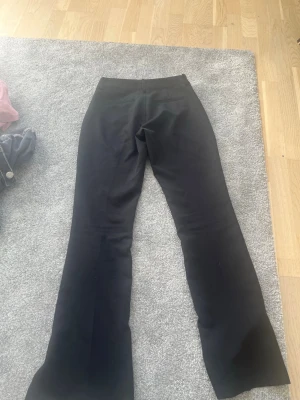 Svarta kostymbyxor från BikBok - Snygga svarta kostymbyxor från BikBok med utsvängda ben och låg midja. Byxorna har en klassisk passform och är perfekta för en stilren look. Materialet känns mjukt och följsamt, vilket gör dem bekväma att bära hela dagen.