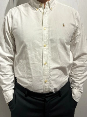 Klassisk Ralph Lauren skjorta - Klassisk vit skjorta från Ralph Lauren med buttons down krage och broderad logga. Amerikansk size 20 vilket ungefär motsvarar Medium. Modell på bilderna är 1,82 och har i vanliga fall size M. Använt men bra skick. Mindre fläck upp till (syns på tredje bilden),  osäker på om den går bort 