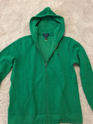 Grön hoodie med dragkedja från Polo - Tjena, säljer denna gröna Ralph Lauren zip hoodien, i ett mycket bra skick. Barnastorlek XL motsvarar herr S. Kontakta vid funderingar.
