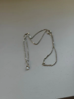 Silverhalsband med klar sten - Snyggt och stilrent halsband i silverfärgad metall med en tunn kedja och ett hängsmycke med en klar, droppformad sten. Perfekt för dig som gillar minimalistiska smycken med en elegant touch.