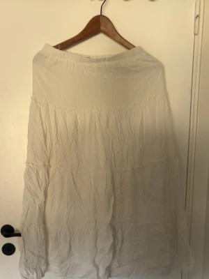 Vit långkjol från Brandy Melville - Säljer en vit långkjol från Brandy Melville med volangdetaljer. Kjolen har en luftig och flowy passform, perfekt för varmare dagar. Resår i midjan för extra komfort och enkel styling.