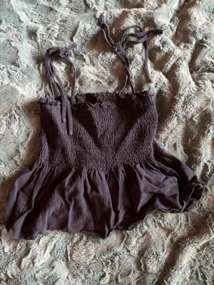 Mörkblå linnetopp med knytband - Supersöt mörkblå linnetopp med smockad överdel och volang nedtill. Axelbanden är justerbara med knyt, vilket ger en personlig touch. Perfekt att styla till jeans eller kjol för en trendig look.