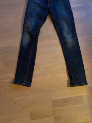 Mörkblå nudie jeans  - Snygga mörkblå slim fit jeans med klassisk femficksmodell och kontrastsömmar. Jeansen har en lätt tvättad look och är tillverkade i denim med stretch för extra komfort. Perfekta för en avslappnad och trendig stil.
