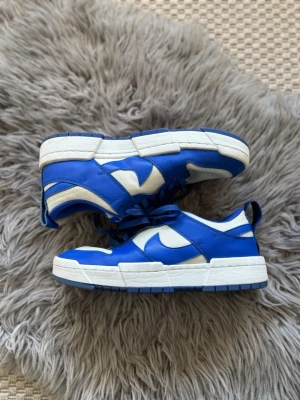 Nike Dunk Low Distrupt Blå och Vita skor - Säljer ett par snygga sneakers från Nike i blått och vitt. Skorna har en chunky sula, klassisk swoosh-logga på sidan och är gjorda i en mix av läder och textil. Perfekta för dig som vill ha en sportig och trendig look.