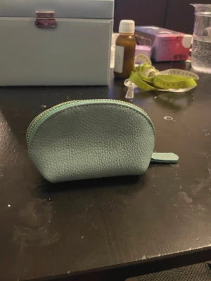 Ljusblå miniplånbok i skinn - Söt ljusblå miniplånbok i präglat skinn med rundad form och dragkedja upptill. Perfekt för mynt, kort eller småsaker. Enkel och stilren design som passar i fickan eller en liten väska.