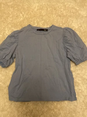 Blå topp med puffärmar - Snygg blå t-shirt med trendiga puffärmar och rund halsringning. Perfekt för dig som vill ha en enkel men ändå stilren look. Inga tecken på användning! Det är bara att höra av dig om du har några frågor eller funderingar💞