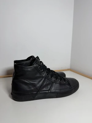 Tremayne high top sneakers Ralph Lauren  - Snygga svarta high top sneakers från RL i äkta läder med svarta skosnören och gummisula. Klassisk design med diskret logga på sidan och stilrena detaljer. Perfekta för dig som gillar en clean och tidlös look.