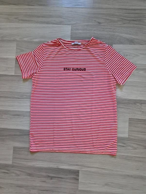 Rödvit randig t-shirt med text - Randig t-shirt från Pieces i rött och vitt med texten 'STAY CURIOUS' broderad på bröstet. Klassisk rund halsringning och korta ärmar. Perfekt för en avslappnad och trendig look.