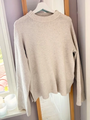 Beige oversized stickad tröja - Mysig beige stickad tröja med oversized passform och bred ribbad kant vid ärmslut och nederkant. Tröjan har rund halsringning och långa ärmar, perfekt för lager på lager och chill vardagsstil.