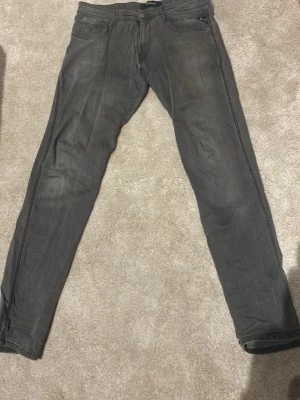 Gråa anbass hyperflex jeans från Replay W32 L34 - Säljer ett par gråa jeans från Replay med klassisk femficksdesign och dragkedja. Jeansen har en slim fit passform och snygga slitningar som ger en cool look. Materialet är mjukt och stretchigt för extra komfort.