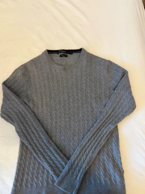 Grå stickad tröja Tiger of Sweden - Snygg grå stickad tröja från Tiger of Sweden i mjuk italiensk ull. Tröjan har ett diskret mönster, rund halsringning och långa ärmar. Perfekt för dig som gillar stilrena och klassiska plagg. Gjord i Italien, bra skick
