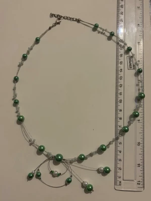 Grönt och vitt pärlhalsband - Stilrent halsband med gröna och vita pärlor på tunn tråd. Halsbandet har flera lager och små transparenta pärldetaljer mellan de större pärlorna. Justerbart spänne i metall. Perfekt för att ge en färgklick till din outfit.