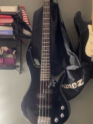 Svart Ibanez elbas, 4-strängad - Snygg svart elbas från Ibanez med fyra strängar och klassisk, rundad kropp. Basen har kromade reglage och detaljer samt en blank finish. Perfekt för dig som vill spela bas i band eller hemma. Medföljer svart gigbag med Ibanez-logga. Möts gärna upp i stockholm!
