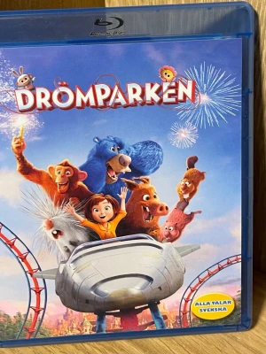 Blu-ray Drömparken (Wonder Park) - Blu-ray-film med titeln Drömparken, ett animerat äventyr fyllt av färgglada djurkaraktärer och berg-och-dalbanor. Omslaget är blått och motivet visar flera djur och en flicka i en åkattraktion. Filmen är på svenska och innehåller extramaterial.
