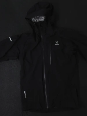 Haglöfs LIM Series vindjacka/regn - Snygg svart regnjacka från Haglöfs med huva och vattentät dragkedja. Tillverkad i slitstarkt Gore-Tex-material och har reflexdetaljer på ärmen. Perfekt för regniga dagar och outdoor-äventyr.