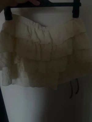 Vit volangkjol med lager på lager - Supersöt beige/vit kort vit kjol med flera volanglager som ger en fluffig look. Har inbyggda shorts som inte syns. 